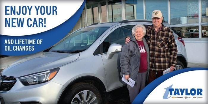A happy couple smiling together, standing in front of a car, sharing a joyful moment.