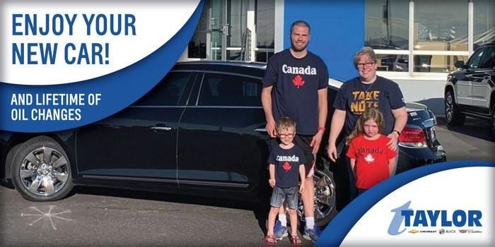 A smiling family of four standing in front of their car